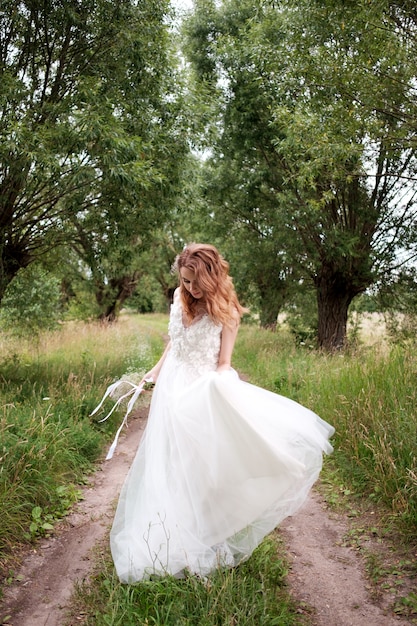 Panna młoda w białej jasnej sukni ślubnej z bukietem ślubnym spacerująca wśród drzew i tańcząca