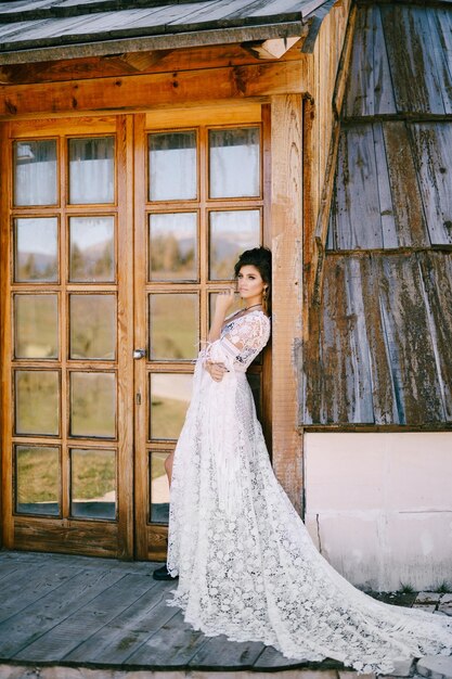 Zdjęcie panna młoda w białej koronkowej sukience przy szklanych drzwiach drewnianej chaty