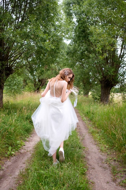 Panna młoda w białej llight sukni ślubnej z bukietem ślubnym ucieka w pasie drzew