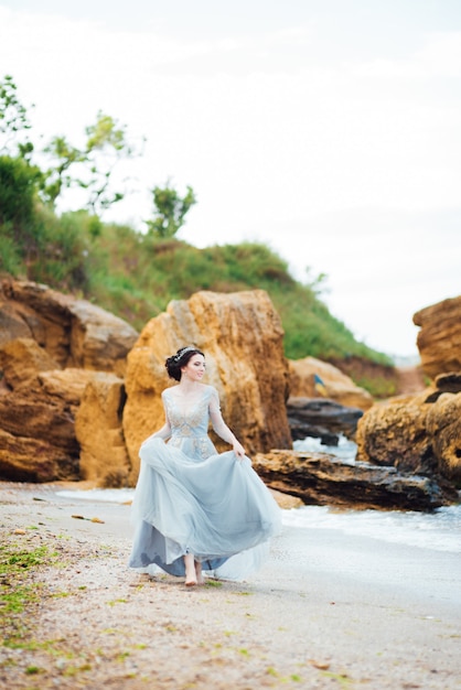 Panna młoda w niebieskiej lekkiej sukience spacerująca wzdłuż oceanu