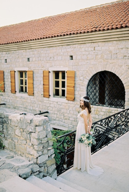 Panna młoda z bukietem stoi na moście w pobliżu kamiennej fortecy