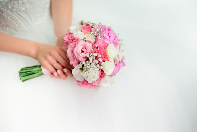 Panna młoda z czułymi rękami trzyma różowego ślubnego bukiet na jej kolanach