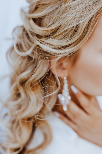 Zdjęcie panna młoda zakłada piękne ślubne kolczyki. dziewczyna z fryzurą z lokami nosi biżuterię
