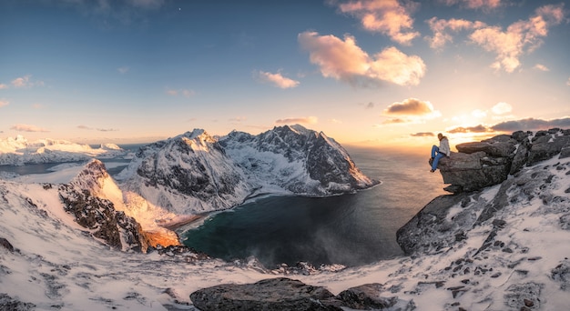 Panorama alpinista siedzi na skale na szczyt góry arktycznego wybrzeża o zachodzie słońca