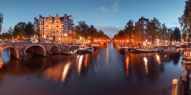 Panorama amsterdamskiego kanału, mostu i typowych domów, łodzi i rowerów podczas niebieskiej godziny wieczornego zmierzchu, Holandia, Holandia. Używane tonowanie