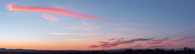 Panorama Dramatycznego Kolorowego Zachodu Słońca Z Ciemnymi I Jasnymi Chmurami. Promienie Słoneczne Przebijają Się Przez Zachmurzone Niebo. Ciemne Chmury Na Tle Jasnego, Nasyconego Nieba.