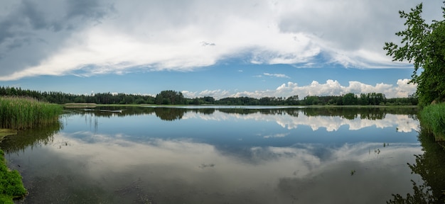 Panorama dublowane błękitne niebo z białymi chmurami i lasem na powierzchni jeziora