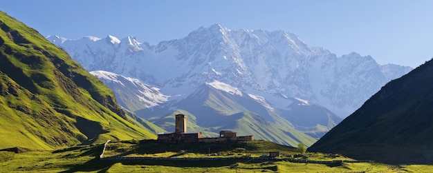 Panorama gór Kaukazu. Kamienny średniowieczny kościół w górskiej dolinie. Widok na górę Szhara. Społeczność Uszguli, Zemo Svaneti, Gruzja