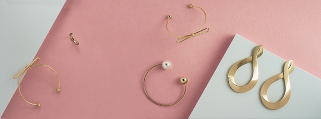 Panorama nowoczesnych złotych bransolet i akcesoriów na różowo-białej powierzchni papieru