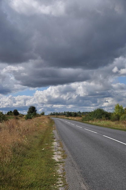 Panorama wzdłuż opustoszałej drogi. Widok na drogę przed deszczem. Chmury na niebie.