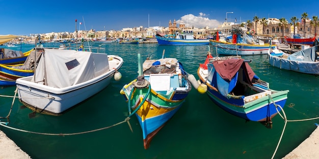 Panorama z tradycyjnymi kolorowymi łodziami Luzzu w porcie w śródziemnomorskiej wiosce rybackiej Marsaxlokk, Malta