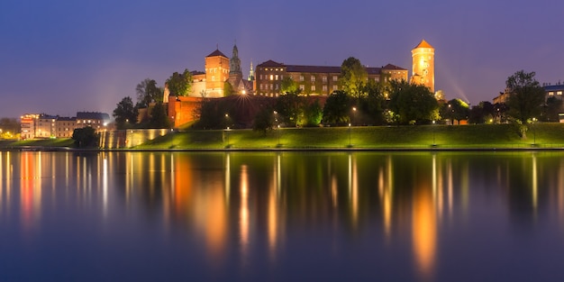 Panorama zamku na Wawelu na wzgórzu wawelskim z odbiciem w rzece w nocy widziana z Wisły, Kraków, Polska