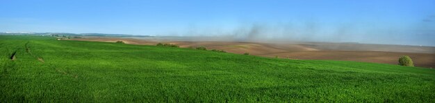 Panorama zielonych pól pszenicy ozimej i kłęby kurzu na pagórkach zaoranych gruntów, burze piaskowe, problem erozji gleby od wiatru