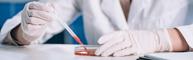 Zdjęcie panoramiczne ujęcie immunologa trzymającego pipetę z czerwonym płynem w laboratorium
