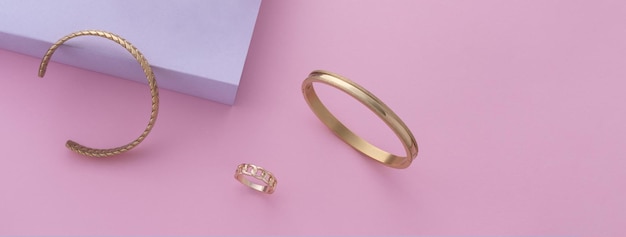 Panoramiczne ujęcie nowoczesnych złotych bransoletek i pierścionka na różowym tle z kopią przestrzeni