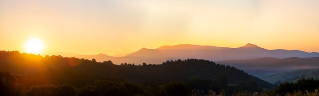 Panoramiczny górski krajobraz z zamglonymi szczytami i mglistą zalesioną doliną o zachodzie słońca.