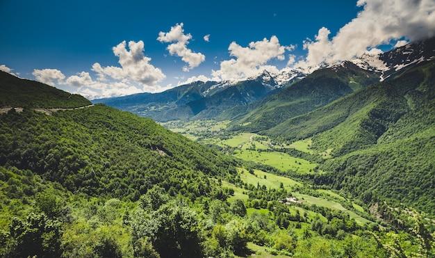 Panoramiczny letni krajobraz z zielonym wzgórzem i górskim szczytem pokrytym śniegiem na tle błękitnego pochmurnego nieba. Region Swanetia, Gruzja. Główny grzbiet kaukaski. Tle przyrody. Wakacje, wędrówki, podróże, rekreacja