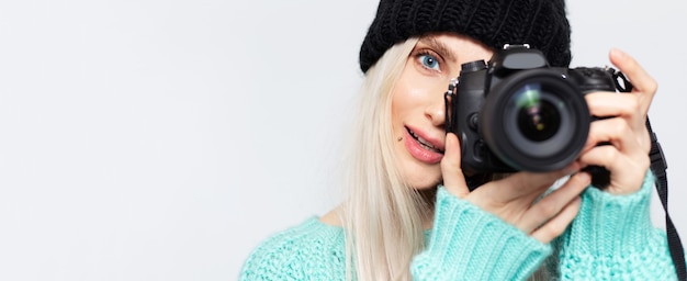 Panoramiczny portret blondynka robienia zdjęć w aparacie DSLR, na białym tle.