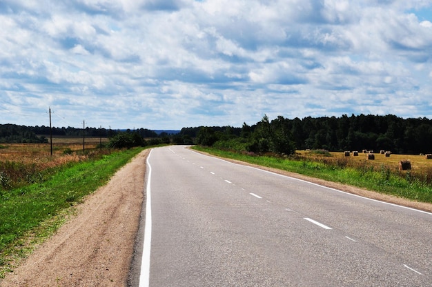 Panoramiczny widok na opustoszałą drogę. Droga biegnie przez pola skoszonej trawy. Przed burzą.