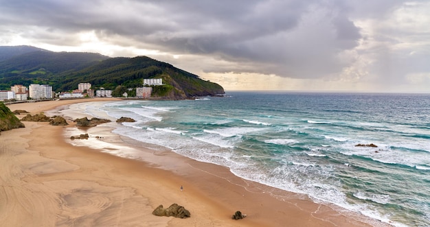 Panoramiczny widok na plażę z falami i górami w pochmurny dzień z deszczem w tle
