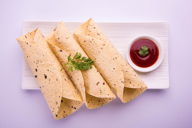 Papad z pieczonej rolki to tradycyjna indyjska potrawa na początek lub dodatek, podawany z keczupem na kolorowym lub drewnianym blacie. Selektywne skupienie