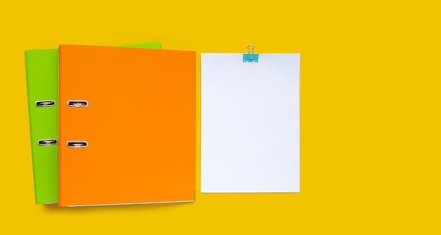 Papier z folderami biurowymi na żółtym tle.