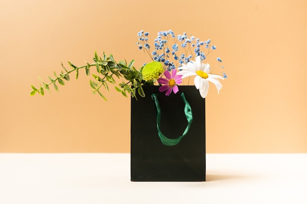 Papierowa torba z pięknymi letnimi kwiatami i roślinami na beżowym tle