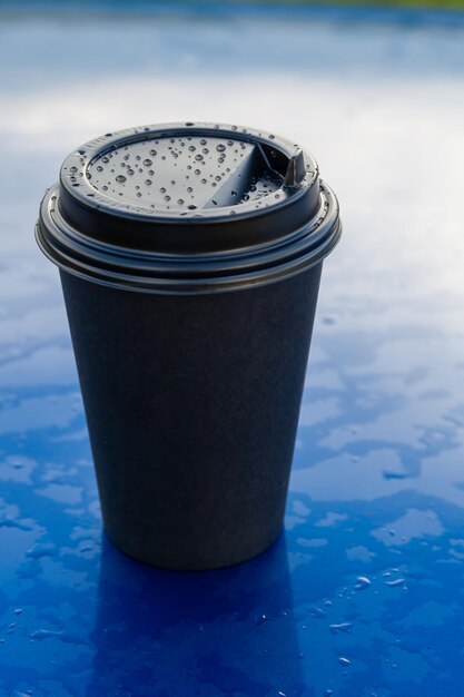Zdjęcie papierowe kubki do kawy na wynos z plastikowymi wieczkami na niebieskim tle z szyną lub kroplami wody na czapce
