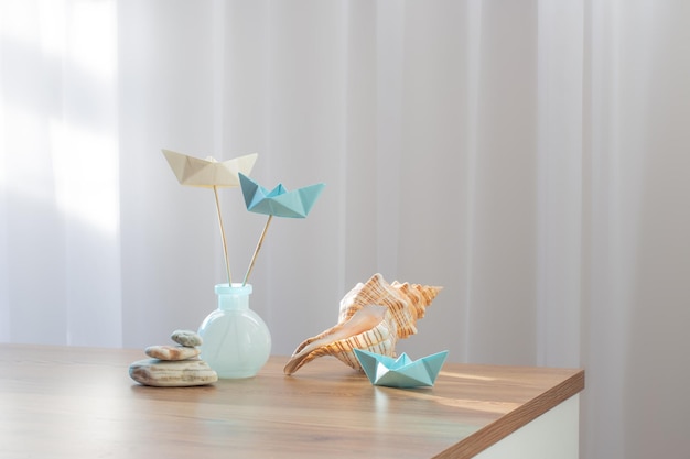 papierowe łodzie w szklanych wazonach z dekoracjami morskimi na drewnianym stole