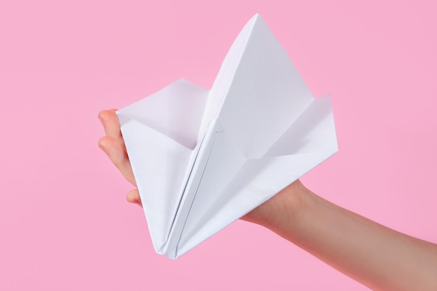 Papierowy samolot w dłoni dziecka na różowym tle gry podróżne z dzieckiem