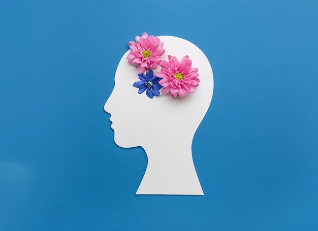 Papierowy symbol ludzkiej głowy i kwiaty na niebieskim tle Koncepcja Światowego Dnia Zdrowia Psychicznego