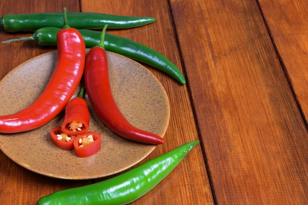 Papryczka chili, podobnie jak jej plastry, leżą na brązowym spodku na tle drewnianego stołu.