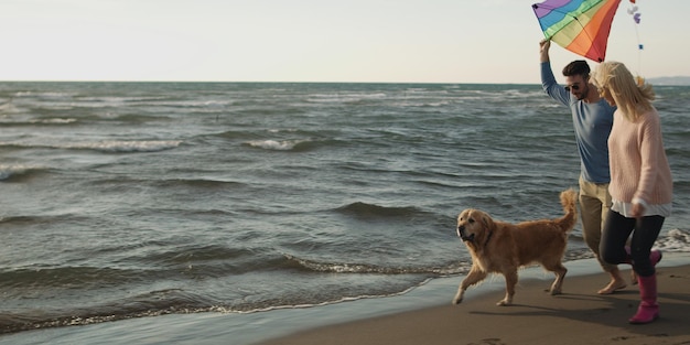 Para biegająca po plaży trzymająca się za ręce z psem w jesienny dzień