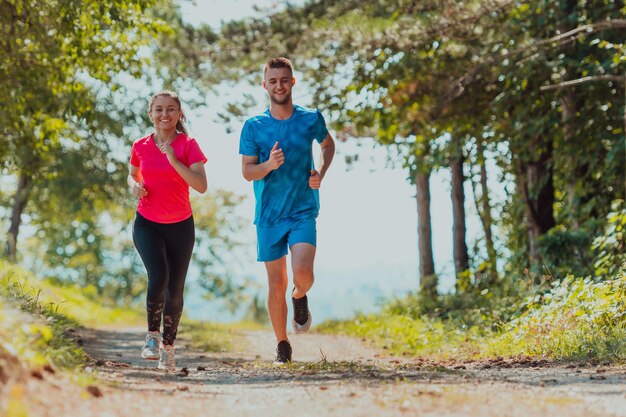 Para ciesząca się zdrowym stylem życia podczas joggingu na wiejskiej drodze przez piękny słoneczny las, ćwiczenia i koncepcje fitness.