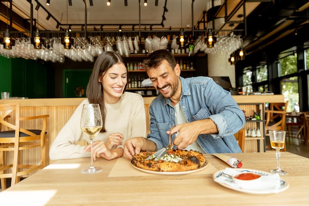 Para cieszy się pysznym posiłkiem w przytulnej restauracji, dzieląc się pizzą i kieliszkiem białego wina