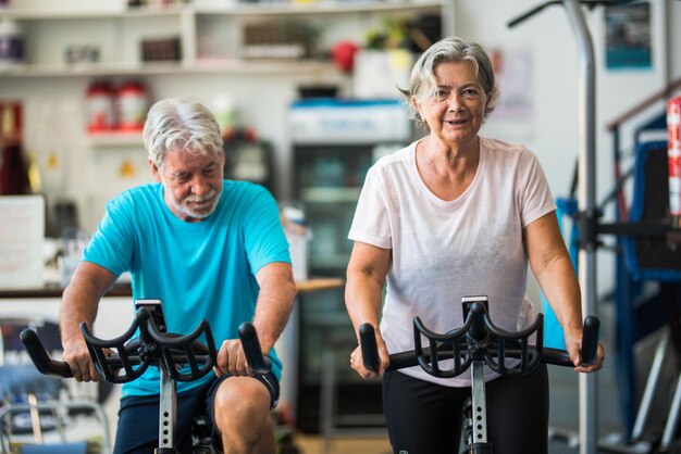 Para dojrzałych osób lub aktywnych seniorów ćwiczących na siłowni, jeżdżących na rowerze w pomieszczeniu, aby być zdrowym, dwoje szczęśliwych emerytów ze zdrowym stylem życia