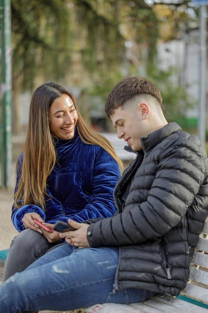 Para dziewcząt i chłopców siedzących na ławce w parku publicznym patrzy na telefon komórkowy