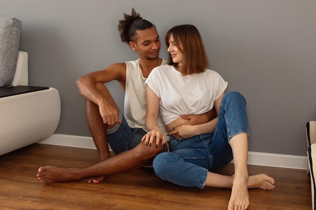 Para facet i dziewczyna siedzą w domu na podłodze przy szarej ścianie