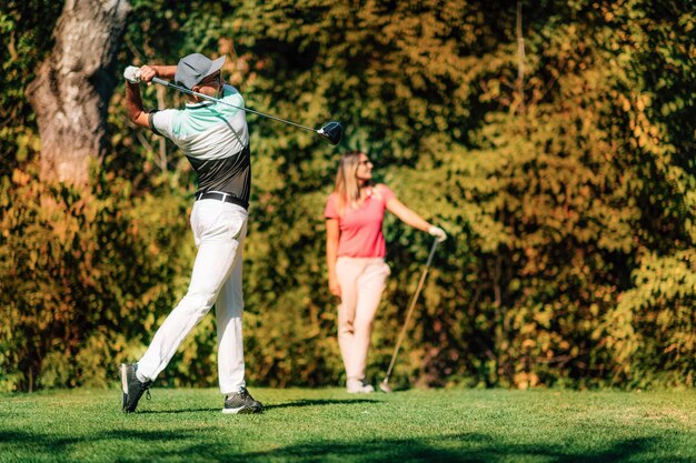 Para grająca w golfa mężczyzna w pozycji huśtawki kobieta podążająca za piłką w locie