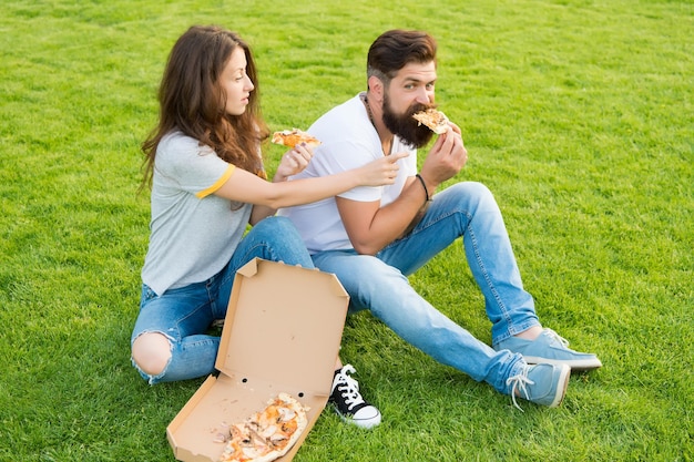 Para je pizzę relaks na zielonym trawniku Szybka dostawa Brodaty mężczyzna i kobieta cieszą się tandetną pizzą Zakochana para spotyka się z pizzą na świeżym powietrzu Głodni studenci dzielą się jedzeniem Czysta przyjemność