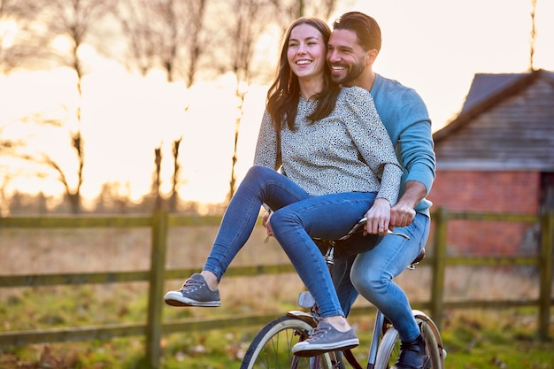 Para jedzie na rowerze po wsi z kobietą siedzącą na kierownicy