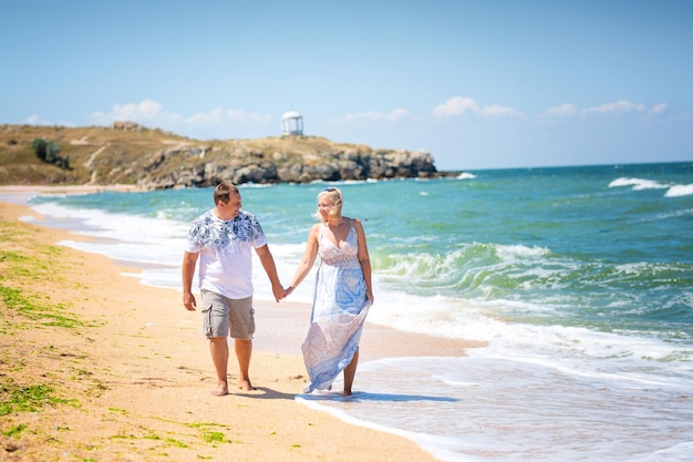 Para kochanków trzymająca się za ręce spacerująca po plaży biegnącej po krawędzi wody widok z przodu