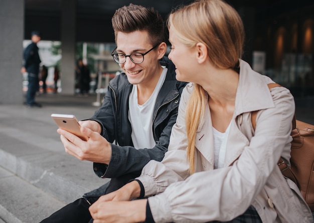 Para lub przyjaciele śmieją się zabawnie i bawią się smartfonem na ulicy dużego miasta.