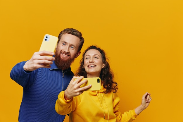 Para mężczyzna i kobieta uśmiecha się wesoło z telefonem w ręku media społecznościowe oglądanie zdjęć i filmów na żółtym tle symbole znaki i gesty rąk freelancerzy rodzinni
