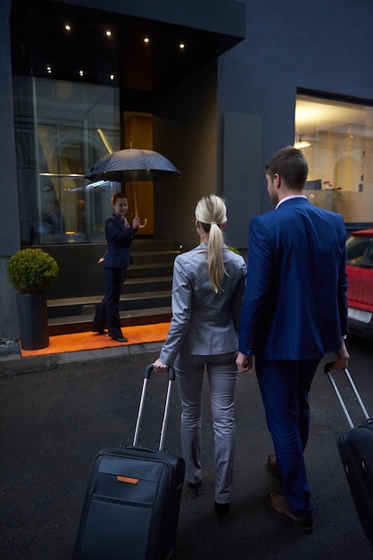 Zdjęcie para młodych biznesmenów wchodząca do hotelu miejskiego, szukająca pokoju, trzymająca walizki podczas spaceru po ulicy