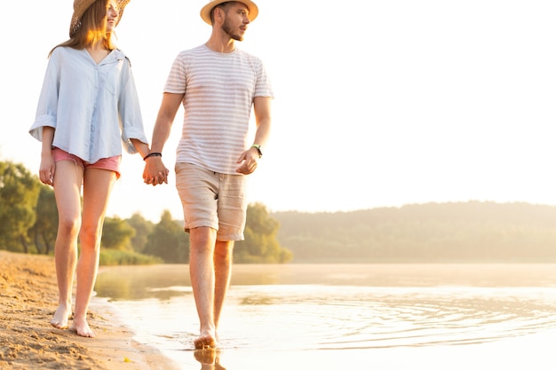 Zdjęcie para na plaży spaceru na romantyczny miesiąc miodowy wakacje lato. młodzi kochankowie szczęśliwy trzymając się za ręce obejmując na zewnątrz.