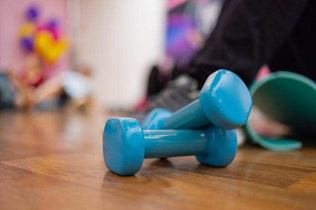 Para niebieskich hantli z twardego plastiku leżących na gumowej matowej podłodze siłowni lub klubu fitness.