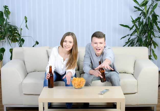 Para ogląda telewizję i pije piwo w domu w żywym pokoju.