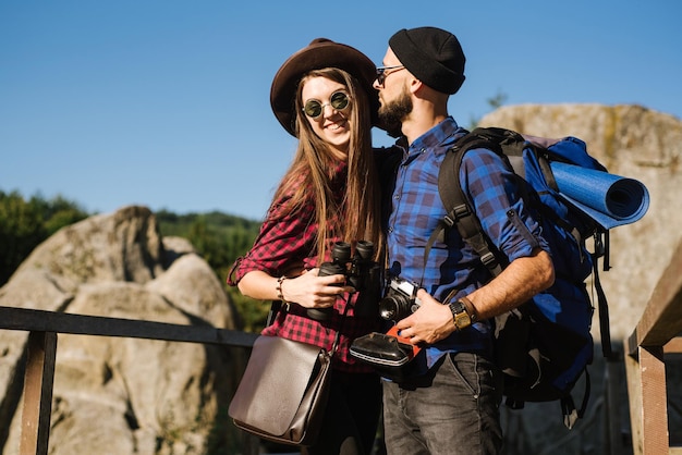 Para podróżująca po górach w hipsterskich ubraniach z plecakiem, zabytkowym aparatem i lornetką
