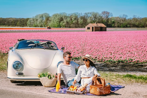 Zdjęcie para podróżująca starym vintage samochodem w holenderskim regionie bulbów kwiatowych z polami tulipanów